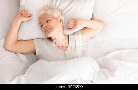 Senior woman lying down in her bed at home Stock Photo