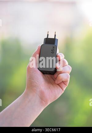 A black network adapter and USB cable for a phone in a man's hand. A charger. Stock Photo