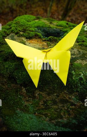 Bright yellow origami butterfly resting on mossy surface, handmade paper art symbolizing creativity, nature and delicate design Stock Photo