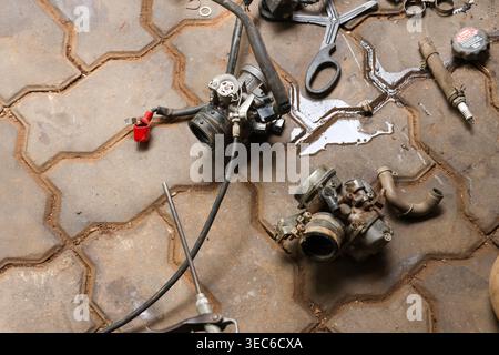 Motorcycle carburetor engine part scattered on brick pavement with wrench tool and spilled oil liquid feeling messy and disorganized during maintenanc Stock Photo
