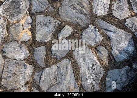 Close up view showing strong and resilient grey stone wall texture background. Rough rock surface pattern features irregular masonry blocks joined by Stock Photo