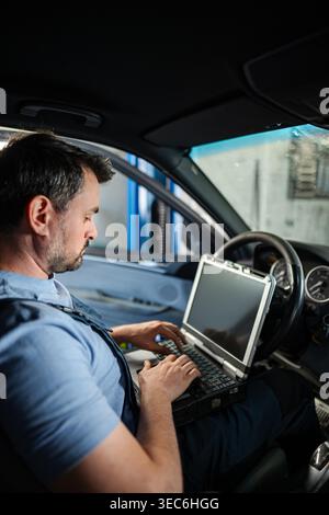 Mechanic running diagnostics on a car using a laptop computer inside a vehicle at an auto repair shop Stock Photo