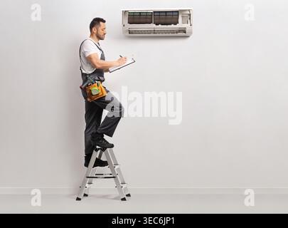 Technician on a ladder checking an air conditioning unit on a wall Stock Photo