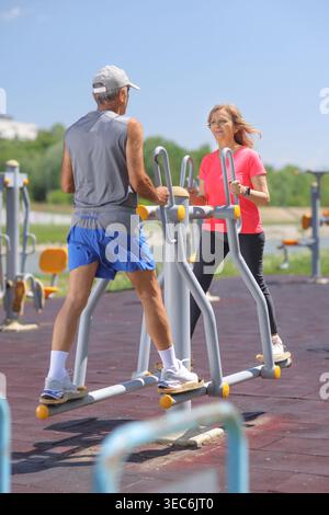 Active senior couple exercising together on outdoor gym equipment in a park Stock Photo