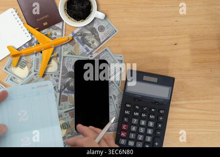 Top view of passport, toy airplane, coffee, smartphone, calculator, passbook and US dollar bills on a desk, illustrating travel budgeting, vacation pl Stock Photo