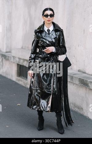 Milan, Italy - 24.09.2021: woman wears black leather trench coat, white dress shirt, black sunglasses, shoulder bag with long black fringe, black heeled boots. Street style look Stock Photo