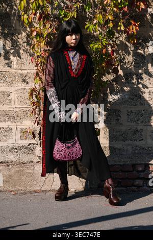 Milan, Italy - 24.09.2021: Susanna Lau wears long black embroidered dress, patterned long sleeve top underneath, brown platform shoes, holding pink Prada Cleo handbag, Prada street style Stock Photo