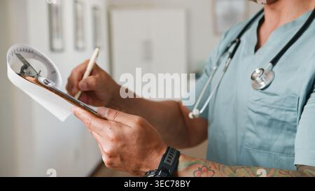 Medical Professional Writing Patient Notes On Clipboard With Stethoscope In Clinic Setting Stock Photo