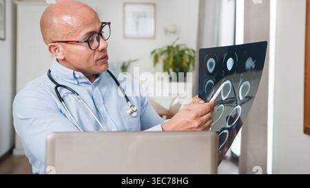 Doctor Examining Brain CT Scans on Laptop During Remote Consultation in Medical Office Stock Photo