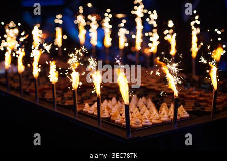 A festive celebration scene featuring rows of mini meringues or cupcakes decorated with burning sparklers creating bright light trails. Stock Photo