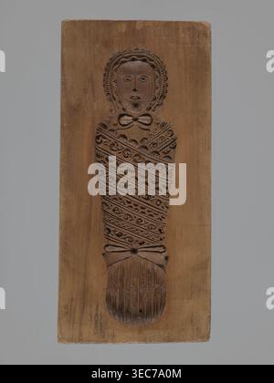 Double-sided gingerbread mould. Obverse: Adam and Eve in paradise; Reverse: baby in swaddling clothes. Gingerbread mould, folk-style decorative and figurative scenes with religious motifs Adam and Eve under the Tree of Knowledge with a snake, plant and floral ornamentation. Rectangular mould, applied/decorative art. Silesia Province of Silesia, 18th–19th century. Height 22.2 cm, width 10.5 cm, depth 3.3 cm., A carved wooden plank with a relief of a wrapped figure is centered against a gray background; the wood shows brown tones with darker carved areas forming a stylized head, face, and body Stock Photo