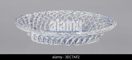 Openwork basket, Ćmielów faience and porcelain factory founded 1804. Openwork basket with an oval, mandorla-like cross-section and parted walls formed by two layers of rollers rotating diagonally in opposite directions. Top enclosed in a band of three rollers; bottom finished in a braided-rope form. Interior bottom fitted with an oval plate. Surface decorated with a blue wallpaper pattern. Abrasions to the glaze and slight chipping on the rim. Dated 1840–1860. Poland; Ćmielów. Ceramic vessel. Height 6.5 cm; length 30.5 cm; width 18.5 cm., A shallow oval woven basket with an open lattice Stock Photo