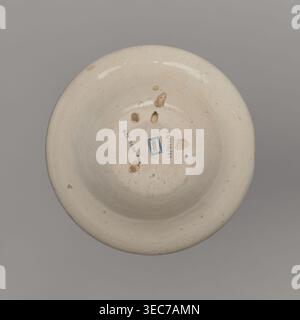 Bowl, unspecified manufacture; mirrors decoration; ; geometric-floral ornament; bowl decorated on the collar with a pattern of triangles and small circles; in the mirror a stylized tulip sprig and three small flower patterns; 18th century, Spain; vessel; height 4 cm, width 18 cm, A round shallow bowl viewed from above with a creamy off-white glazed surface showing a few irregular brownish chips and spots on the interior and rim, a group of small circular and oval indentations toward the center, a small rectangular blue patch near the middle, and a plain gray background surrounding the object. Stock Photo