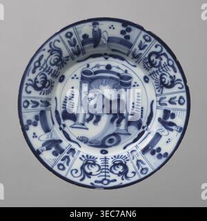 Plate, De Porceleyne Claeuw faience manufacturer; 1658–1840 manufacturer, animals, lions, plant decorations, chinoiserie. Semi-deep plate, quite thick-walled with a collar thinner at the edge. On a light blue background, decoration in dark cobalt. At the bottom, between two arbor posts flanked by schematically outlined bushes, a standing lion with a human face. The collar features six trapezoidal segments separated by narrow vertical fields with floral decoration, three of which depict a seated male figure, the other three arranged alternately with a schematic, symmetrical volute-floral Stock Photo