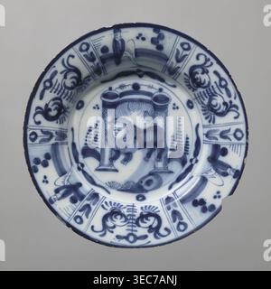 Plate, Lambertus Sanderus 1764-1806 author; De Porceleyne Claeuw faience manufacturer; 1658-1840 manufacturer. Semi-deep faience plate, quite thick-walled with a collar thinner at the edge. On a light blue background, decoration in dark cobalt. At the bottom, between two arbor posts flanked by schematically outlined bushes, a standing lion with a human face. The collar features six trapezoidal segments separated by narrow, vertical fields with floral decoration, three of which depict a seated male figure, the other three arranged alternately with a schematic, symmetrical volute-floral Stock Photo