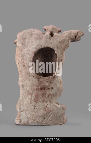 Figurine of Eros with a lyre, Eros myth., Greek deities, lyres musical instruments. Figurine of Eros standing on a base, holding a lyre resting on a base. 2nd century BC, Southern Italy . Terracotta figurine, height 19 cm, width 13.5 cm, depth 4.5 cm, weight 0.38 kg., A weathered sculptural object resembling a hollow form with an irregular rounded opening in its front, showing a rough, textured surface; the piece has an overall dusty pinkish-beige color with areas of light gray and pale brown, and a slightly darker interior visible through the opening; its silhouette includes a protruding, Stock Photo