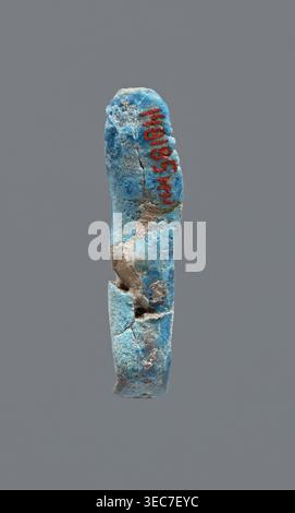 Shabti, mummy-shaped figurine, funerary gift. Legs missing. Arms crossed on the chest. Hands invisible from under the shroud. Smooth tripartite wig on the head. Facial details invisible. Not inscribed. Late Period, 664–332 BC, Egypt. Height 3.7 cm., A broken elongated object with a rough, pitted surface suspended against a plain gray background, showing a predominantly blue coloration with areas of pale blue and turquoise, patches of beige and tan where material is missing, and small dark gray spots; the object has visible cracks and holes, an irregular rounded top and a fractured lower Stock Photo
