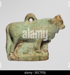 Amulet — bull; figurine of a bull standing on a base, full-plastic work with a pendant on the back; modeled quite carefully. Late Period, Egypt, 664–332 BC. Amulet; height 2.5 cm, width 3.1 cm., A small sculpted object in the shape of an animal is shown against a plain pale gray background; the object appears worn and has an overall greenish hue with areas of light blue-green and patches of beige and brown discoloration; the animal form includes a rounded body, a raised head with a blunt snout, a short tail, and four legs standing on a flat rectangular base, and there is a circular hole near Stock Photo
