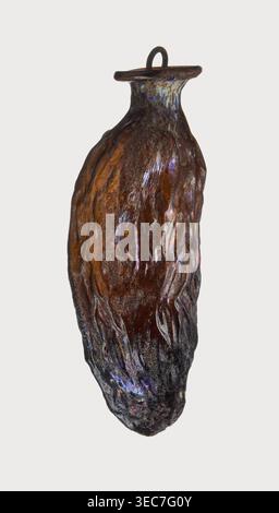 Date-shaped unguentarium; Syro-Palestine workshop; Smyrna place of discovery; 1st–beginning of 2nd century AD; Type: Isings form 78D. Translucent amber glass, inclined rim with inwardly curved edge; blown in a two-part mold. Rim diameter 2 cm; height 8.15 cm; belly diameter 2.95 cm; weight 0.020 kg., A single elongated object with an irregular, textured surface resembling a vessel or pod, predominantly brown with areas of dark brown and black; the surface shows iridescent highlights in purple, blue, and hints of green and pink; the top narrows into a short neck with a flat, circular rim and a Stock Photo