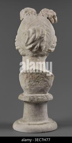 Head of the goddess Aphrodite, Roman workshop, Roman sculpture portrait, early 1st century AD, sculpture; restitution Przeworsk; Aphrodite mythology., The image shows the rear view of a weathered stone bust on a round pedestal against a plain dark gray background. The bust has textured, carved hair gathered at the back with visible waves and folds, and the stone surface displays uneven wear and pitting. The pedestal and lower portion of the bust share the same mottled stone appearance with areas of lighter and darker beige, off-white, pale gray, and subtle brownish tones. The overall color Stock Photo