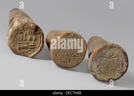 Mentuemhat's funeral cone, Mentuemhat ca. 700–650 BCE. Clay cone with hieroglyphic inscription arranged in four lines on the base; inscription includes name Nesiptah. Late Period, Western Thebes grave 34 on Asasipha, cone grave. Height 8.5 cm, width 12 cm, weight 0.628 kg. Davies-Macadam, Corpus No. 486, 664–332 BCE., Three cylindrical objects lie on a flat surface, each showing a round carved end facing the viewer. The left object is a weathered beige-brown with a circular carved design and darker shadowing along its side. The middle object is a rough tan color with a textured circular face Stock Photo