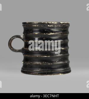 Dice cup. Small cup with a flat slightly concave bottom, slightly tapered walls, distinct rim and foot. Outer surface decorated with seven wide ribs; bottom has concentric decoration. Entire object covered with black varnish shiny but matte in places; traces of turning visible under varnish. Spout slightly chipped; surface shows dirt and secondary losses; varnish worn on rib ridges. Clay color 5 YR 6/6 reddish yellow; varnish color 2.5 YR 2.5/1 black. Dice game. 5th century BC, Attica. Vessel cup. Height 8.3 cm; width 10.6 cm; depth 8.3 cm., A worn black ceramic mug with a round handle on one Stock Photo