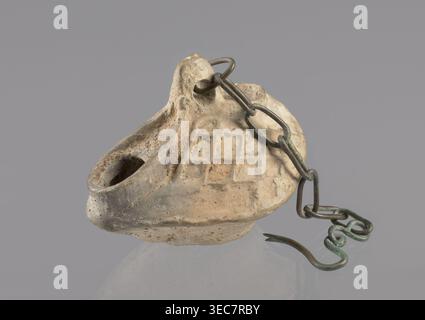 Lamp, repossession Ząbkowice Śląskie, Egypt, Coptic art, antiquity, oil lamps, Middle Ages. Oval lamp made of yellow-gray clay with a high container and two handles, through which a bronze chain is strung for hanging the lamp. The high, sloping arms are decorated with a plastic ornament of a rectangular mesh. A channel running perpendicularly through the arms from the handle reaches the wick hole and surrounds it, creating a high rim. 5th/6th century, Egypt, oil lamp, height 10 cm, width 7.1 cm, An off-white to beige clay oil lamp with a textured, grid-like pattern on its top surface and a Stock Photo