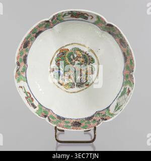 Bowl, ceramics, figural scenes, knightly scenes, Chinese art, Chinese culture, colored porcelain, backdated signatures, six-leafed, bottled belly. Porcelain body; white, transparent glaze. Decoration painted with overglaze enamel paints and iron red. 19th century, China, vessel. Height 6.5 cm, diameter 20 cm., ., A shallow scalloped ceramic dish on a metal stand with a white interior and exterior, featuring a central circular medallion containing a stylized creature and cloudlike forms in green, orange, yellow, gray, black, and a touch of blue, surrounded by a thin gold ring; the rim area has Stock Photo