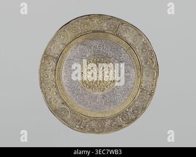 Mirror frame, 19th century, possibly Turkey or Iran. Metal; weight 685 g, diameter 25.5 cm, height 1.2 cm. Islamic art mirror frame with plant motifs and geometric ornament, featuring a 6-pointed star Solomon's Seal and stylized plant patterns arranged geometrically., A circular ornate metal plate with intricate filigree and embossed floral patterns, showing a central rosette with layered petal-like openwork, surrounded by concentric bands of detailed vine and leaf motifs; the plate displays a mix of metallic gold and silver tones, with areas of darker shadowing and light reflecting off the Stock Photo