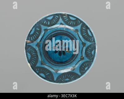 Plate, Islamic art, Persian culture, ceramics, plate/saucer, Caucasus, geometric motifs, decoration: black painted semicircles, stylized flower in the mirror, 17th century, Azerbaijan, vessel, height 2.0 cm, diameter 12.5 cm, A round ceramic plate with a glazed surface in shades of blue and dark teal, featuring a central floral-like motif surrounded by concentric circular bands and a repeating scalloped decorative pattern along the rim; the glaze shows visible crack lines and some small chipped or worn areas, and the background behind the plate is a flat neutral gray. Stock Photo