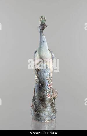 Peacock figurine, Chinese, Qing 1644–1911, 19th century; ceramics, colored porcelain; subject: peacock with peacock-feather ornament, plum trees, tree trunks, flowers; sculpture; height 54.5 cm, width 14.0 cm, depth 12.5 cm, weight 2.9 kg., A ceramic sculpture of a stylized bird perched on a textured trunk is shown against a plain gray background, the bird featuring a long neck and a small crest with eye-shaped details; the surface displays a mix of pale green, light blue, soft pink, muted purple, and touches of brown and beige, while the trunk shows darker blue-gray and brown tones with Stock Photo