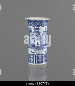 Flute-type vase, blue-and-white porcelain, Chinese, 17th–18th century, height 15 cm, diameter 8.1 cm; decoration: landscape motifs., A cylindrical ceramic vessel with a flared rim stands upright against a plain gray background; the vessel is primarily white with blue painted decorations depicting architectural shapes and decorative borders, including a darker blue scalloped band near the top, a scene of pagoda-like structures and a walled gate around the middle, and a patterned border with floral motifs near the base; the surface shows glossy reflections and a faint mirror-like reflection of Stock Photo