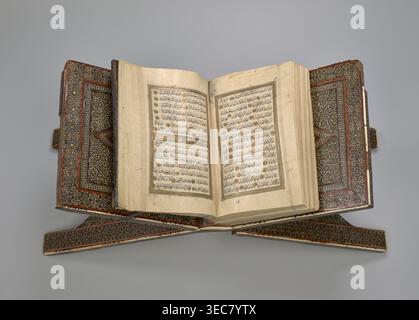 Quran lectern rahla, Islamic art, Persian art, Qajar dynasty 1785–1925, geometric ornament, stands, rahla, Quran, Persian culture, 19th century, Iran, piece of furniture; unfolded: length 21.5 cm, width 41.4 cm; folded: length 41.5 cm, width 16.5 cm, An open ornate book rests on an intricately decorated wooden stand, showing two facing pages with dense lines of dark script surrounded by rectangular decorative borders; the book cover and stand feature repeating geometric and floral patterns in shades of brown, red, gold, black, and white, while the pages are aged beige with some darker spots Stock Photo