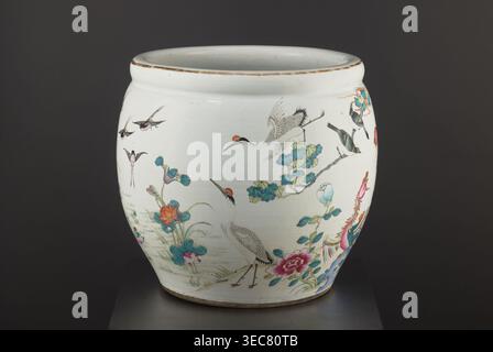 Pool - aquarium, Chinese, Qing dynasty 1644–1911, 19th century. Porcelain colored decoration with chrysanthemums, lotuses and birds. Bulging vessel narrowed at the bottom; height 41.5 cm, diameter 41.1 cm. Function: aquarium/ornamental pool., A rounded ceramic vessel sits against a dark background, predominantly white with painted decorative scenes. The vessel shows a group of birds including cranes with red crowns and a few smaller birds in flight, rendered in shades of black, gray, and white with red accents. There are floral and foliage motifs around the base and sides in colors including Stock Photo