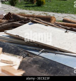 Close-up of a messy pile of renovation debris outdoors. Old white doors, wooden logs, and cardboard sit in a heap under bright sunlight. Focus on text Stock Photo