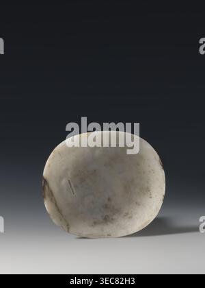 Convex plaque, Chinese, Taoism, Immortals iconography, Qing dynasty 1644–1911, white bluish jade, bas-relief, 19th century, China; plaque, height 12.0 cm, width 10.5 cm., A rounded, shallow stone object with a smooth surface showing mottled patches of off-white, gray, brown, and beige sits centered against a dark gradient background transitioning from deep charcoal to lighter gray toward the bottom, casting a soft shadow to the right. Stock Photo