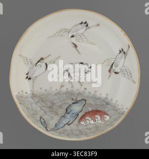 Plate. Chinese; Qing dynasty 1644–1911. Porcelain fragment with white glaze, decoration painted with overglaze enamel paints depicting cranes and waves. 19th century. Vessel. Height 2.8 cm; diameter 13.5 cm; weight 0.15 kg., A round ceramic plate with a pale cream background and a thin light brown rim, decorated with a scene of a group of white cranes with black feather accents and small red markings on their heads, depicted in various flying and standing poses. The lower portion shows stylized pale green and grey wave patterns, a bluish rock-like shape, and a rounded red form with white Stock Photo