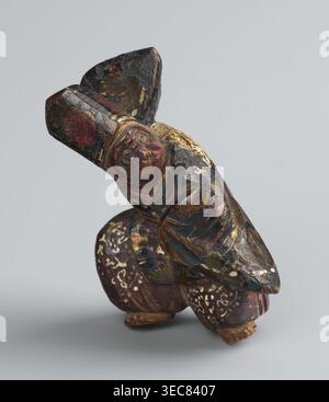Netsuke in the shape of a sanbasô dancer;, Japanese, Edo period 18th century; material: carved netsuke figurine; subject: ritual dance, dancer wearing a mask; dimensions: height 6.3 cm, width 4.0 cm., A small carved figure with a rounded face and pronounced features wearing a tall hat is shown in a crouching pose; the surface shows worn paint in black, deep red, muted gold, brown, and touches of green, with areas of flaked and chipped finish revealing lighter wood beneath, and patterned white speckles on the rounded lower portion, all set against a plain light gray background. Stock Photo