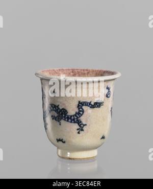 Bowl, Chinese, 19th century. Blue-and-white porcelain with cracklework decoration depicting dragons, pearls, and flames. Rolled edge and small foot; crackled glaze stained with pink and lilac spots. Vessel; height 7.7 cm, diameter 7.9 cm., and provenance., A small ceramic cup with a rounded body and short foot, shown against a plain light gray background, has a crackled off-white glaze with a warm beige and faint pinkish tint, and a few areas of darker beige spotting; a hand-painted dark blue sinuous dragon motif wraps around the body with several small dark blue decorative marks scattered Stock Photo