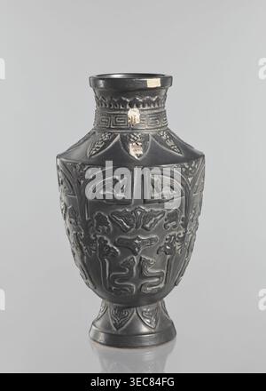 Vase, Japanese, Meiji–Taisho periods late 19th–early 20th century; 1st half of the 20th century. Ceramic decorative vessel from Kagoshima, Japan. Vase on a slightly widening foot with clearly defined shoulders and a short neck; dark brown glaze; decorated with meander, plant and animal motifs; signed. Height: 42 cm., A dark vase with a matte black surface sits against a light gray background, showing a rounded body that tapers to a narrow neck and flared rim and rests on a short pedestal base; the vase is decorated with raised, carved motifs forming symmetrical panels of stylized animal and Stock Photo