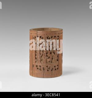 Brush vessel, Chinese, Qing 1644–1911, early 20th century. Porcelain container with bas-relief reserves depicting figural scenes in a landscape and images of birds. Height 16.4 cm; diameter 11.9 cm., A cylindrical wooden object with a warm brown tone sits against a neutral gray background; its surface features intricate openwork carvings depicting a scene with human figures and stylized trees, surrounded by carved decorative borders and repeating patterns, and the wood shows natural grain variations and some darker and lighter brown areas. Stock Photo