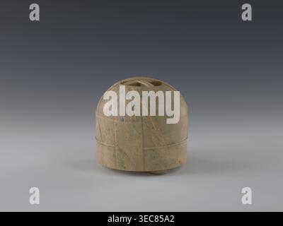 Tin with lid, gift, Chinese art, Chinese culture, Qing 1644–1911, yurts, 19th century, China, container; height 12.8 cm, diameter 13.1 cm, A rounded, dome-like object sits centered on a smooth surface against a gradient background that transitions from dark gray at the top to lighter gray near the bottom. The object is made of a mottled stone with a mix of tan, beige, brown, and hints of green-blue veining. Its surface shows carved lines and shallow grooves forming curved and vertical bands around the form, and there is a shallow recessed opening at the top. The base rests on a small circular Stock Photo