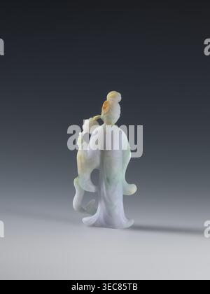 Taoist goddess?;, Chinese; Qing dynasty 1644–1911; Taoism; flowers iconography; scepter; green-pink slightly translucent jade; 2nd half of the 18th century; figurine sculpture; height 17.1 cm, A small carved figurine of a robed person seen from behind, standing on a flat surface against a dark gray to light gray gradient background, rendered in pale colors including white, light green, light purple, and touches of orange; the figure has a high hairstyle and holds a curved object with floral-like details, with flowing sleeves and a flared hem creating soft, rounded shapes and subtle shadowing Stock Photo