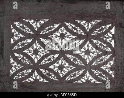 Katagami dyeing stencil with a motif of overlapping circles shippô. Ise-katagami stencil, chuban format. Pattern: geometric motif—rhombuses inscribed in ellipses with stylized floral rosettes in the rhombuses. Late 19th century Meiji period, Japan. Stencil katagami. Height 41.0 cm, width 31.5 cm., A rectangular patterned fabric with a dark gray background and white cutout areas forming a repeating geometric floral motif, featuring a grid of diamond shapes each with a central flower-like element surrounded by petal-shaped cutouts and curved leaf-like arcs; the dark gray fabric shows visible Stock Photo