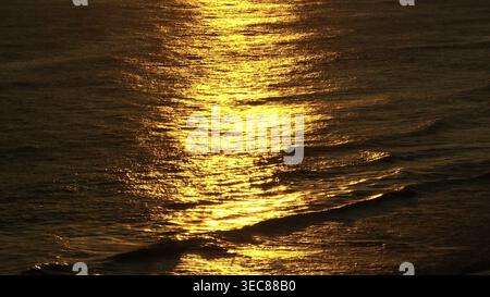 Golden sunlight gently reflecting on surface of dark ocean water and small waves, creating a shimmering, texture pattern during sunset at Bukit Peninsula, Bali. Natural background rise up panorama Stock Photo