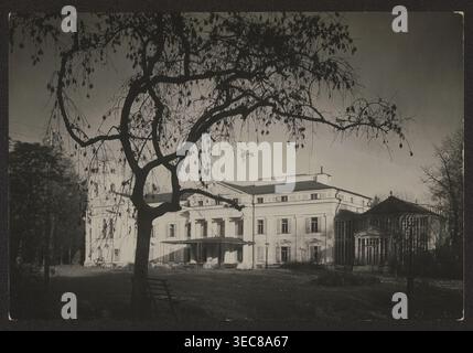 Werki — palace facade; photographer: Jan Bułhak 1876–1950; subject: palaces in Werki Lithuania, Tyszkiewicz family residence; noted by Mieczysław Orłowicz 1881–1959; circa 1934; location: Vilnius; nature photography; dimensions: 11.3 × 16.9 cm., A large dark tree with many thin hanging branches and sparse leaves dominates the foreground, its silhouette contrasting against a lighter sky; a simple wooden bench sits near the tree trunk. Behind the tree, a grand multi-story building with a classical facade and columned portico extends across the scene, flanked by a glass-roofed conservatory on one Stock Photo