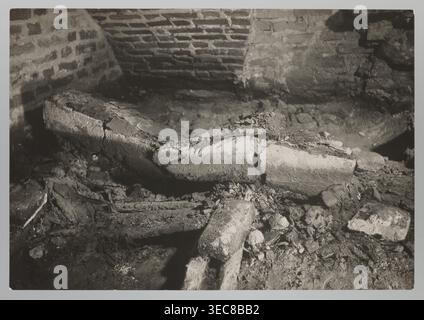 Vilnius. Cathedral �� interior of the royal crypt, photographed by Jan Bu?hak 1876�C1950, Archcathedral Basilica of St. Stanislaus and St. Ladislaus Vilnius, crypts, archaeological excavations after the 1931 flood in Vilnius, 1931. Photograph; natural photography. Image size: 11.5 cm �� 16.7 cm., The image shows a dim interior scene with a rough brick wall in the background and a broken, curved stone or concrete structure lying among rubble in the foreground. The surface textures include cracked and crumbling masonry, loose debris, and scattered fragments of rock and mortar. Lighting is low and Stock Photo