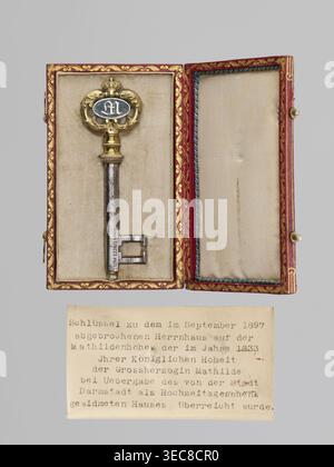 Rectangular key case with a hinged lid and two clasp hooks. Trimmed with red leather, with gilded embossing; on the lid, a frame along the edge with an ornament in the corners. In the centre, a ducal mitre. On the underside, a gilded frame along the edge, in the centre a non-gilded embossed rhombus with an inscribed quatrefoil, and in the centre a rhombus with a four-petal rosette. Glued on a printed card with inventory numbers numbers added in ink. Inside, a typewritten note describing presentation of the key in 1833. Date: 1833. Place: Darmstadt, Germany. Varia. Dimensions: height 9.8 cm, Stock Photo