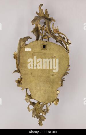 Cartel clock by Franciszek Gugenmus 1740–1820, 2nd half of the 18th century, Poland Warsaw. Bronze wall clock so-called cartel with rocaille and floral motifs; bronze casing without traces of gilding, possibly also made in Warsaw. White enameled dial with black Roman numerals, signed Fcois GUGENMUS / A VARSOVIE. Back covered with a brass sheet with rectangular doors. Mechanism not signed; pendulum missing. Height 80 cm, width 38 cm., A decorative metallic object photographed against a neutral light background, showing an ornate back with flowing, scroll-like floral and leaf forms and a smooth Stock Photo