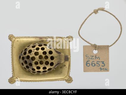 Toothpick holder, hedgehogs, animals, tassels. Bronze toothpick holder in the shape of a pig resting on a rectangular base bordered with a fringe. 1820s–1840s, Poland . Varia. Height 3.5 cm; width 6.3 cm; depth 4.7 cm., A metallic object with a golden color sits on a square golden base with decorative rounded corners; on the base rests an oval perforated piece with many round holes and some darker areas of patina. To the right, a small square tag made of brown paper hangs from a loop of coarse beige twine; the twine forms a loop with a knot at the top. The background is a very light gray. Stock Photo